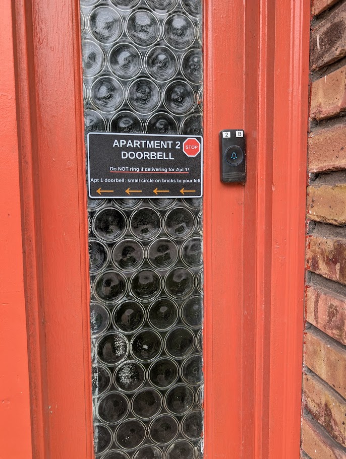 SignAptics apartment doorbell sign mounted on a property door, with delivery instructions and directional arrows